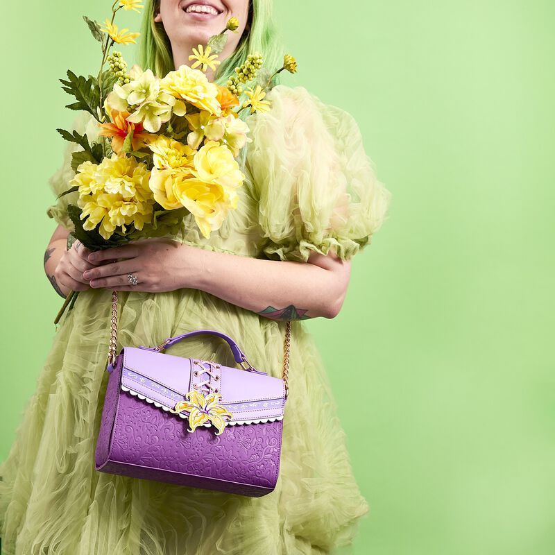 Woman wearing a green-yellow dress against a green background, holding a bouquet of flowers, and wearing the purple Rapunzel crossbody